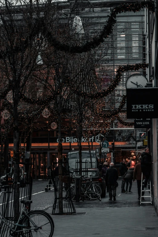 some people are walking on the street near trees and shops