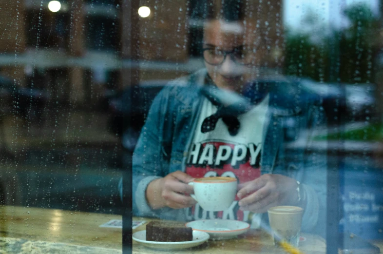 a man eating cake and smiling as he sits at a table in front of a window