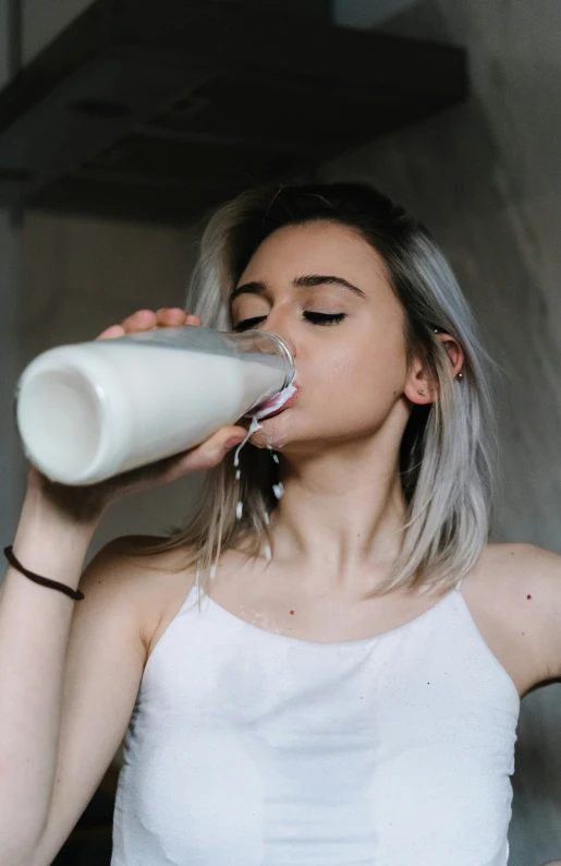 woman drinking from a white cup while standing by the wall