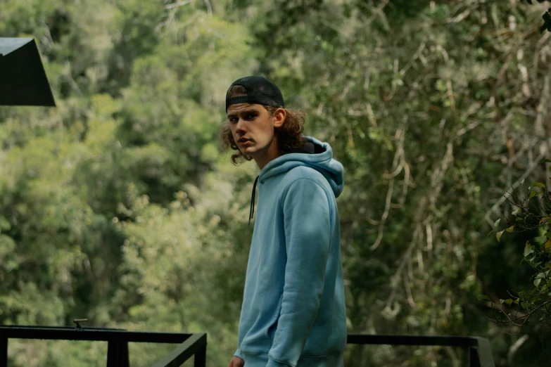 a young man standing near a forest filled with trees