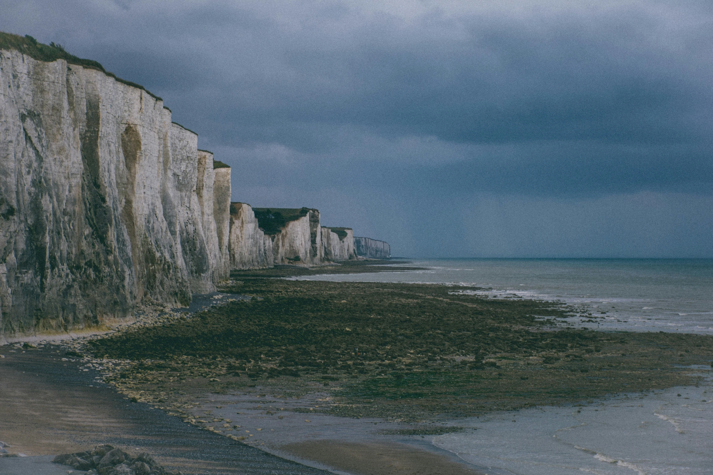 the cliffs are next to the sea and grey clouds