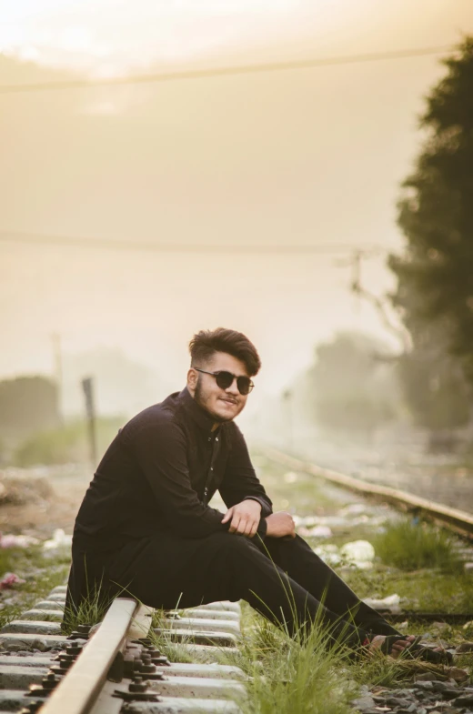 a man poses while sitting on a train track