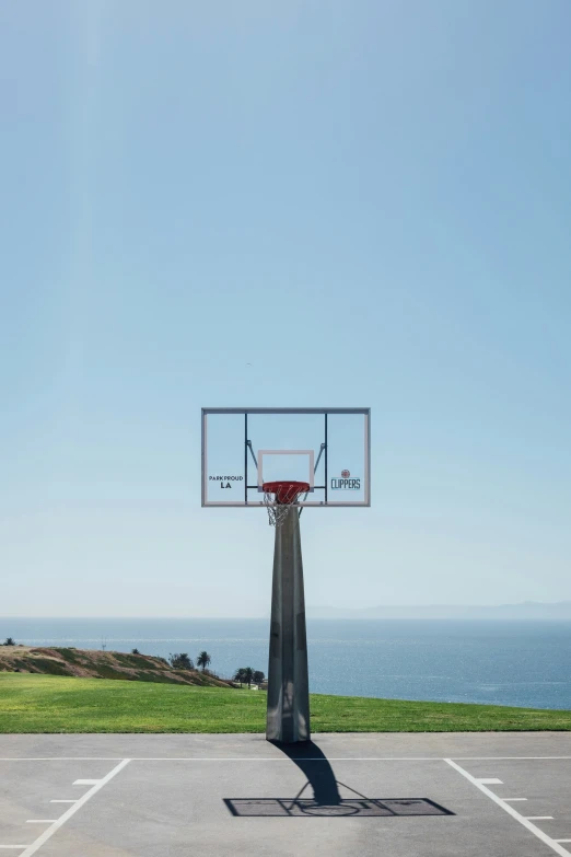 basketball hoop at the top of the basketball court with ocean view in background