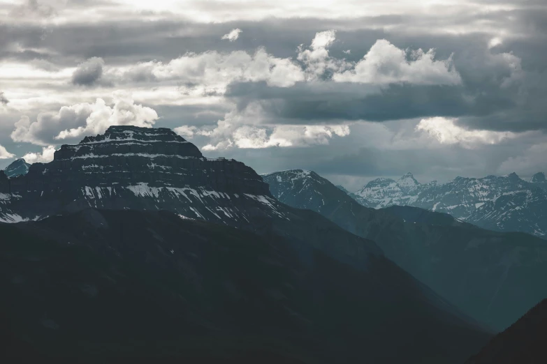 a mountain range with some snow on it and clouds in the sky