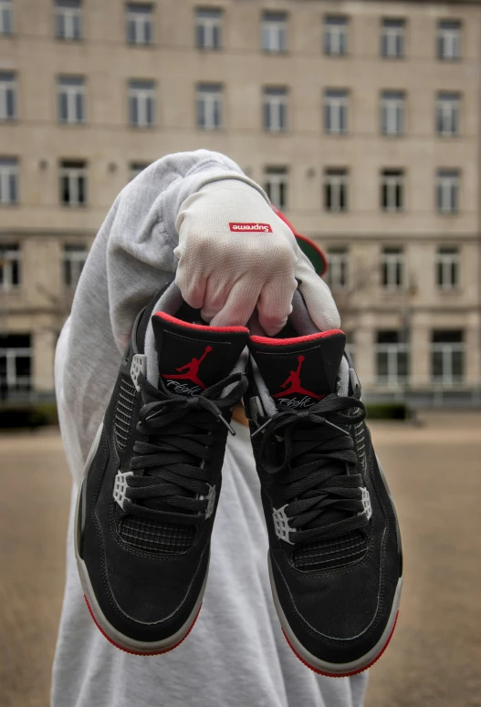 a man holding up two pairs of black and red jordan shoes