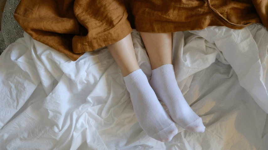 a woman laying in bed with white socks and brown blanket