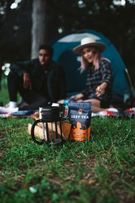 a person sitting on the ground by a tent with camping supplies