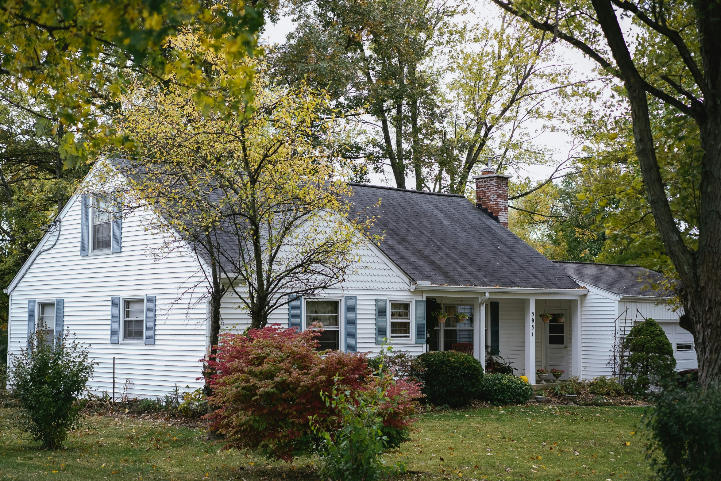 a white house with two windows in front of some trees