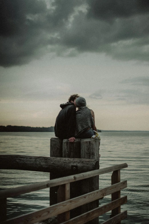 two people sitting on top of each other near the ocean