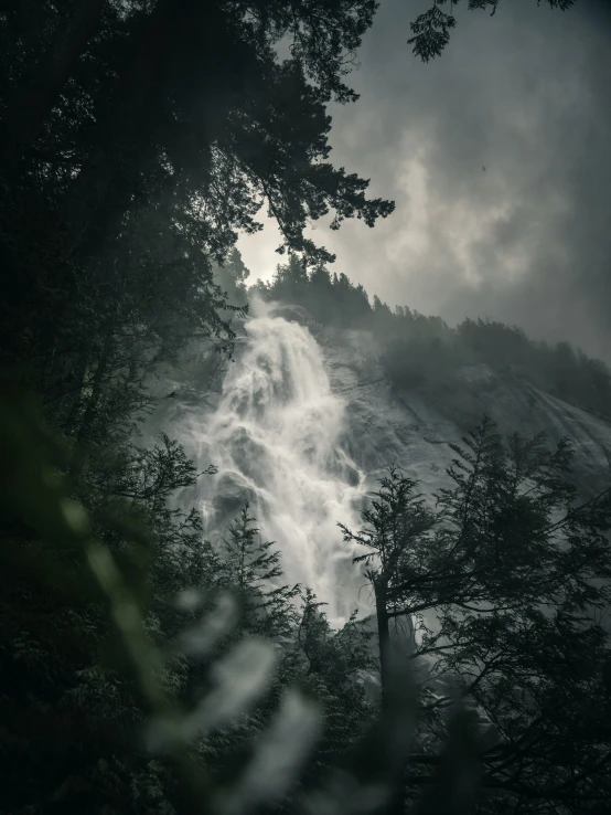 a mountain with trees in the foreground is lit by low - key rays from dark clouds