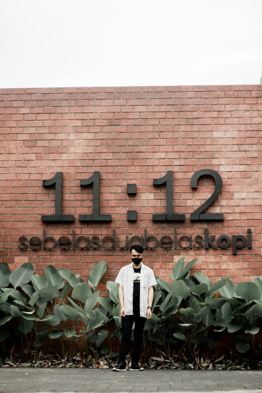 person in sunglasses standing against a wall near large bushes