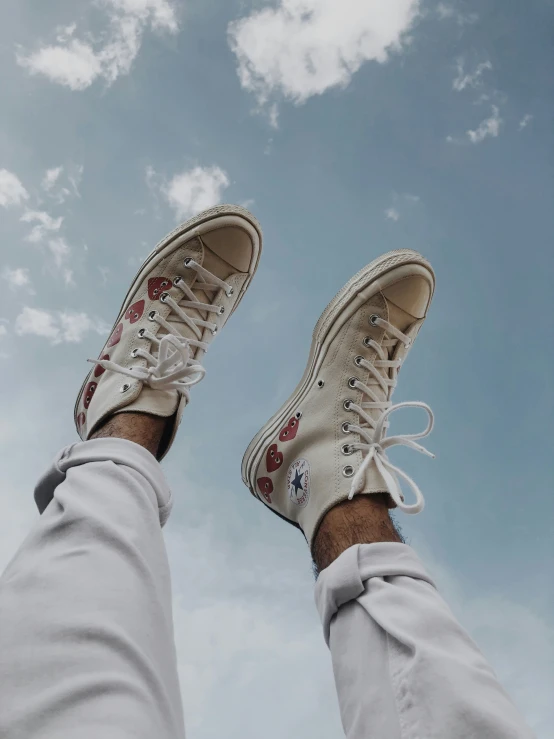 a man is wearing white sneakers while standing under the blue sky