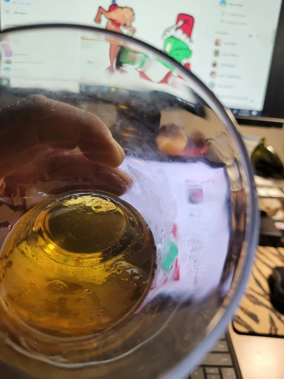 someone is holding their drink glass by the computer