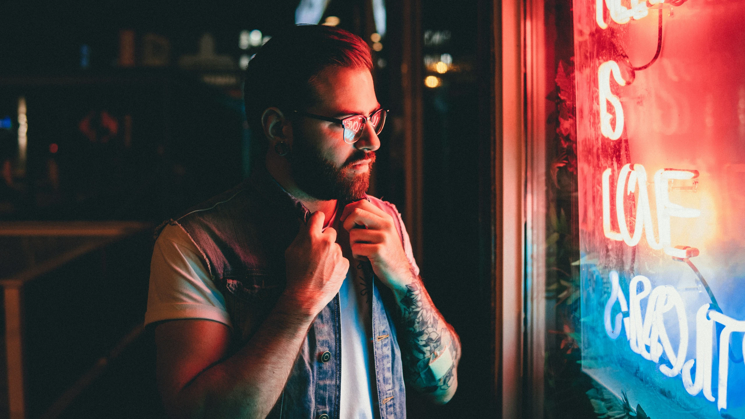 man wearing glasses adjusting his tie while looking out a window