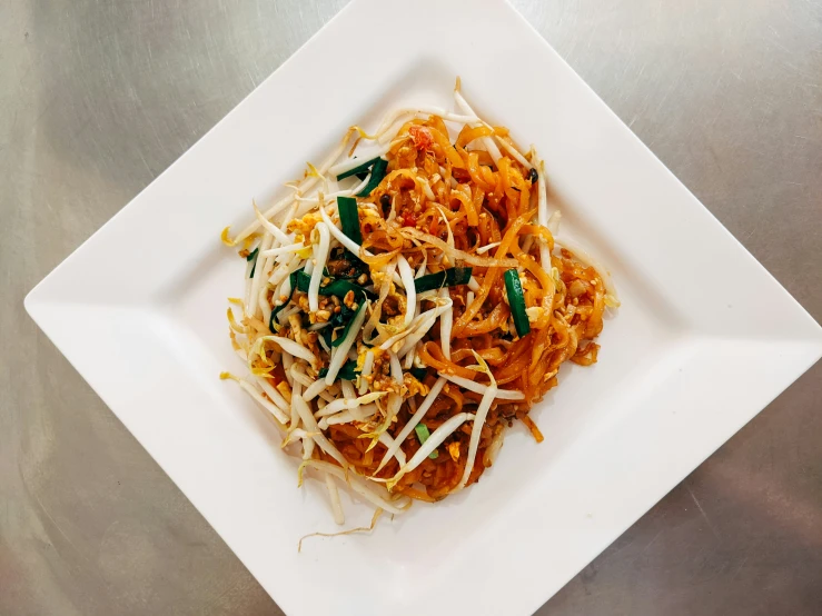 a white square plate filled with pasta, cheese and green leafy onions