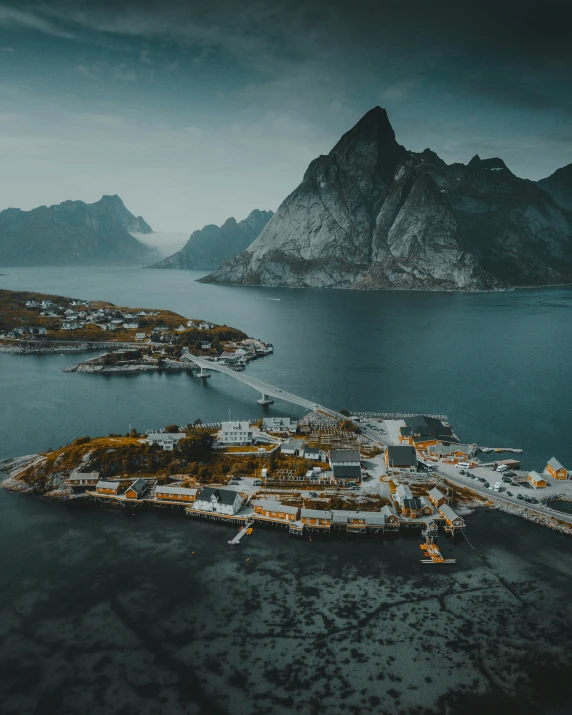 an island surrounded by mountains and water under a cloudy sky