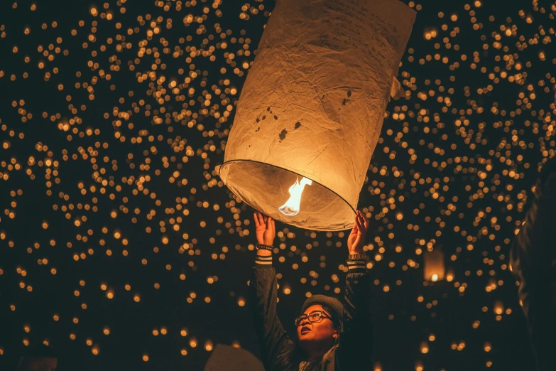a woman is holding a paper lantern that is lit up in the night