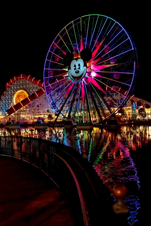 a lighted ferris wheel at night with people watching it