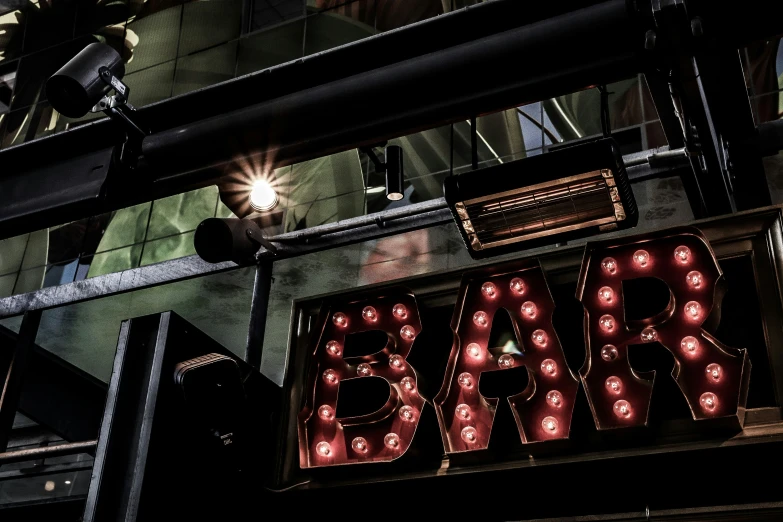 bar sign with lights underneath it near the sidewalk