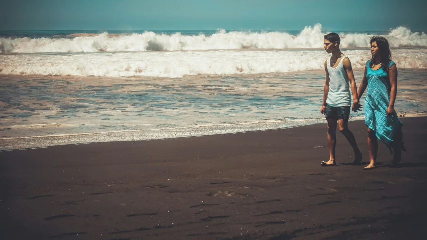 a man and woman holding hands while walking on the beach