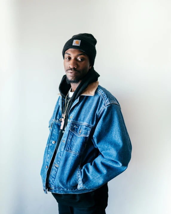 a man in a denim jacket leaning against a wall