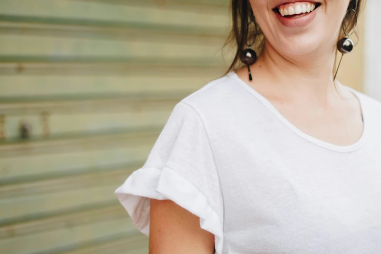 a woman smiling wearing black earrings next to a window