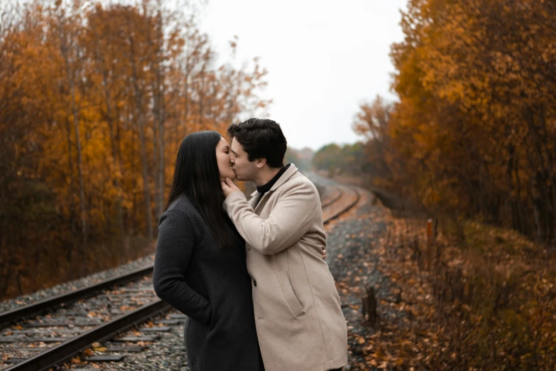 two people kissing by train tracks in the autumn