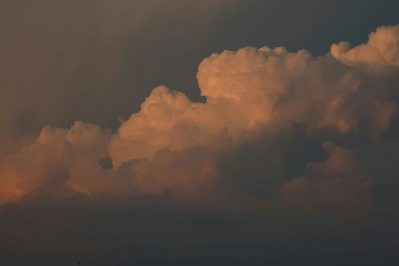 a jet airliner flying in between several clouds at sunset