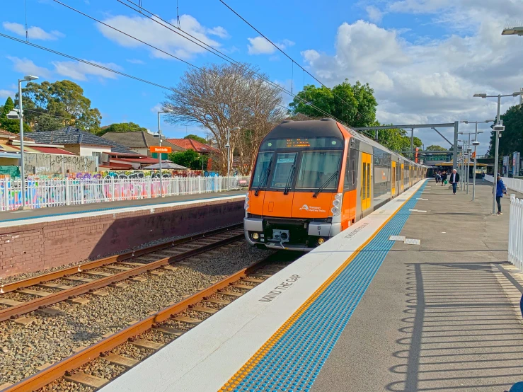 an orange train traveling down train tracks next to a sidewalk