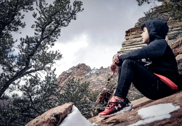 a young man sitting on a rock and looking up at the sky