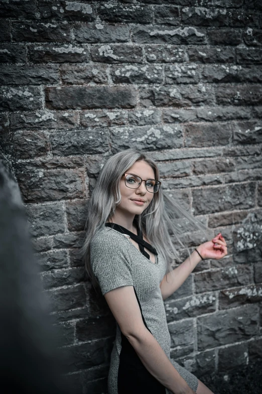 a woman wearing glasses standing next to a brick wall