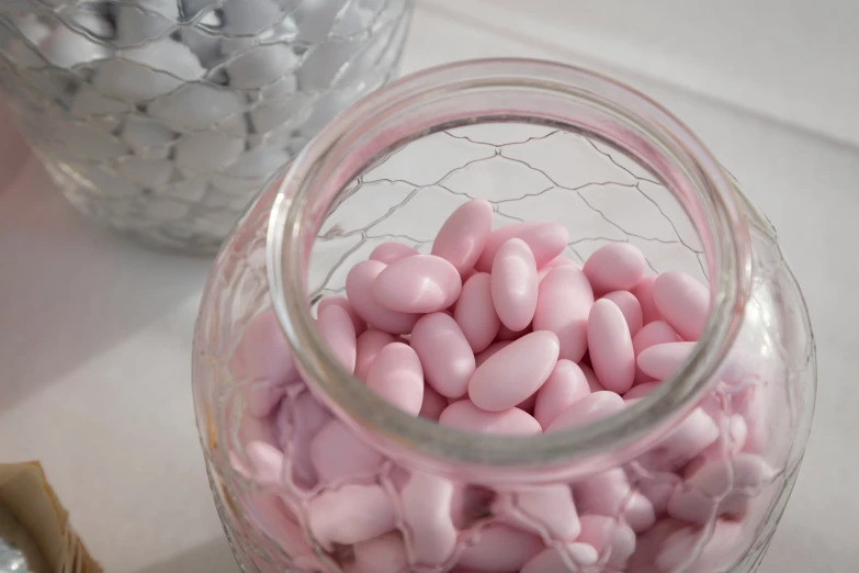 a jar full of pink and white candy next to an empty jar