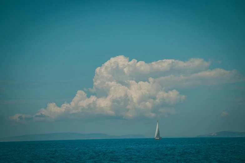 a sailboat is on the open water with many clouds in the background