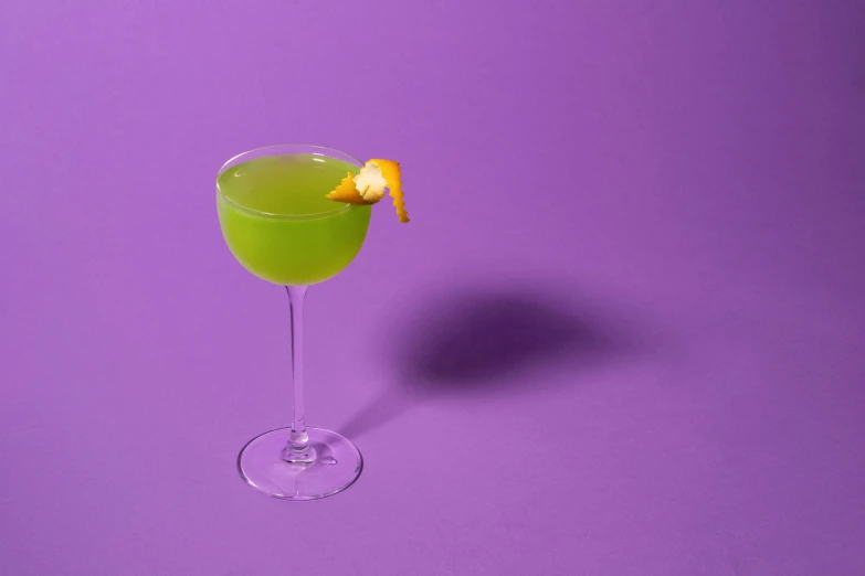 a green drink with an orange peel in the glass