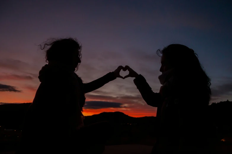 two woman with their hands in the shape of heart