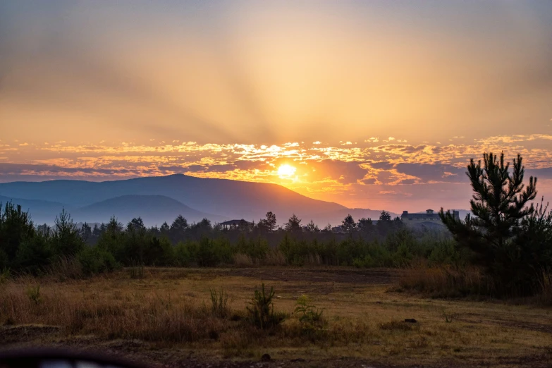 the sun rising behind the mountains and trees