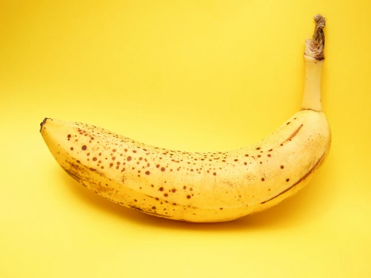 a ripe banana with red spots sitting on a yellow background