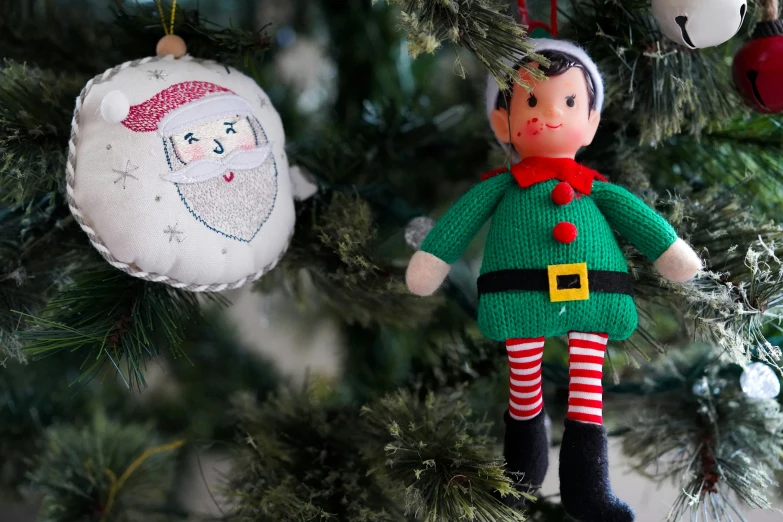 a christmas ornament on top of a pine tree with a toy elf hanging from it