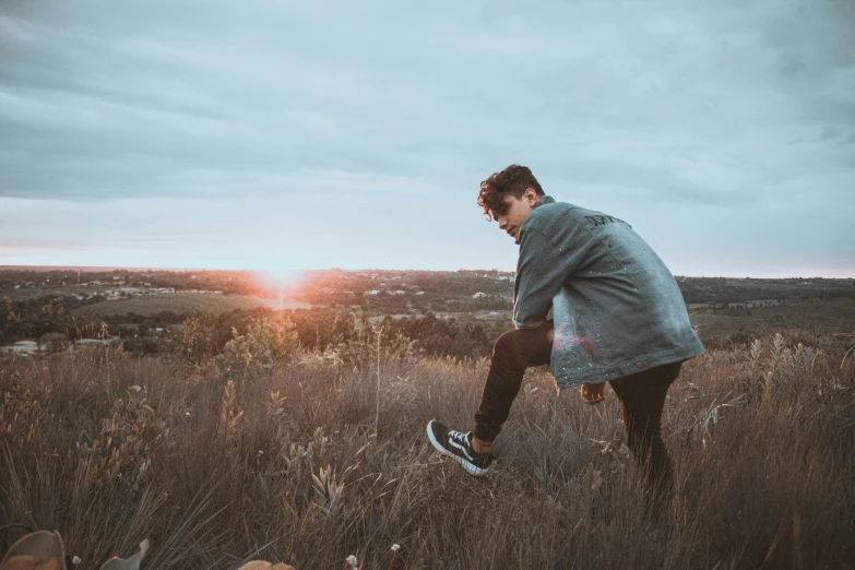 man wearing jacket and standing in grass at sunset