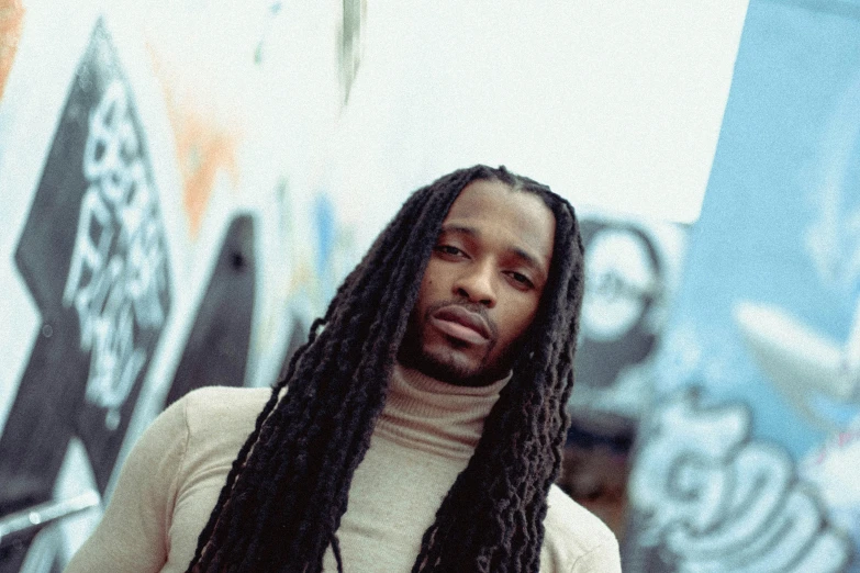 a man with dread locks stands next to a wall