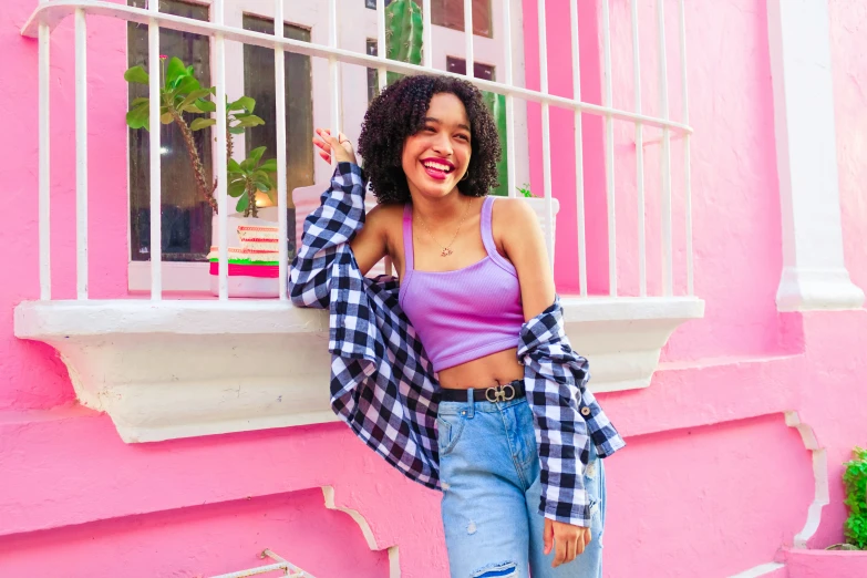 a woman in plaid jacket and ripped jeans leaning against pink wall