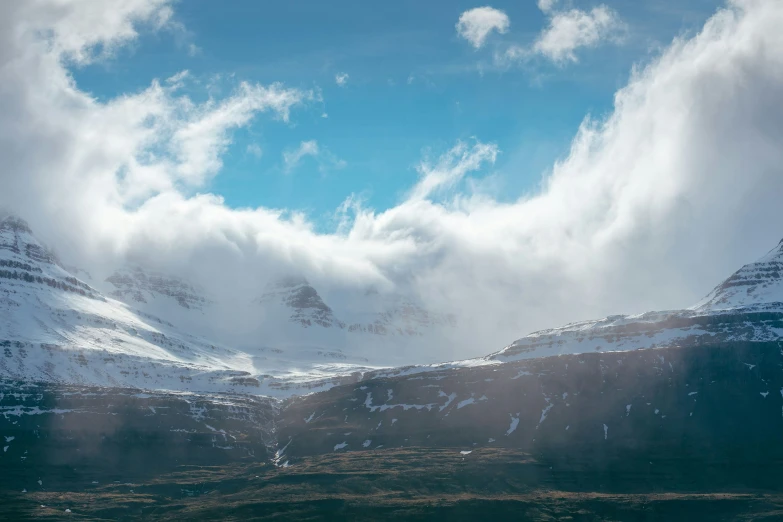 several mountains with snow covered tops under a blue cloudy sky