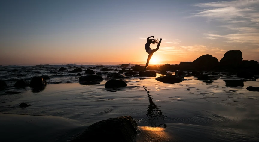 a man doing yoga on rocks near the ocean