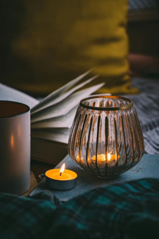 an open book sitting next to a small candle and a white cup