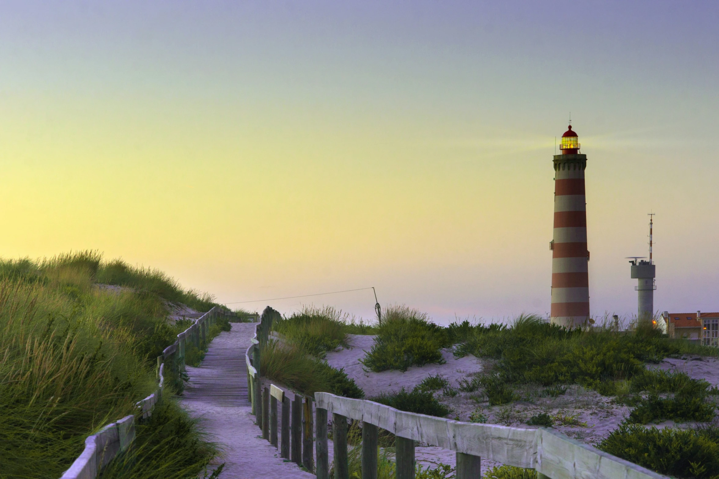 there is a small lighthouse at the edge of a grassy path