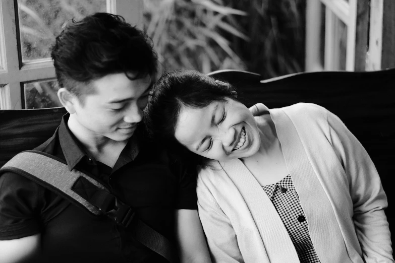 a young man laughs while sitting next to an older woman