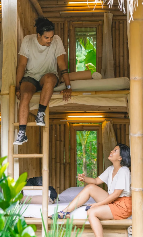 a man and woman sit on bunk beds in a bamboo house