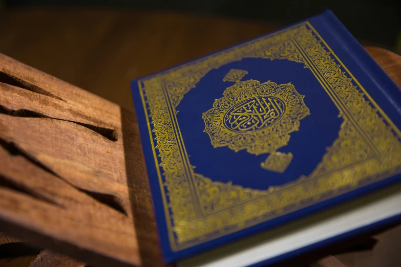 a blue book with an illuminated arabic name is shown on wood