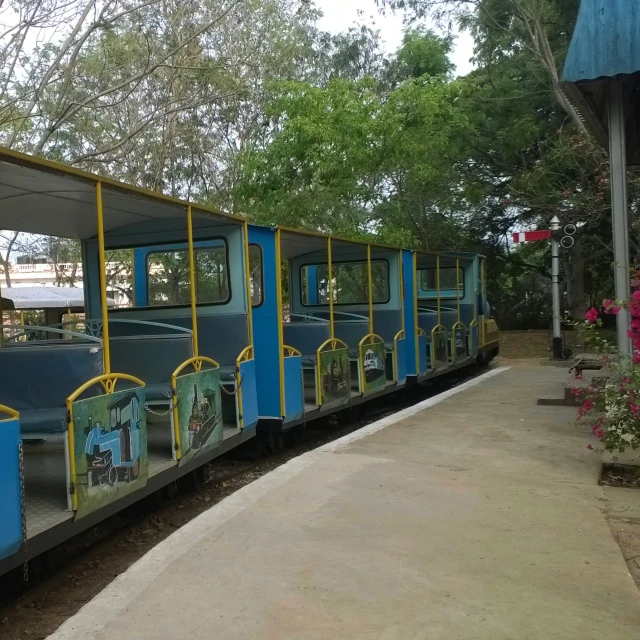 a blue train passing through a tree covered park