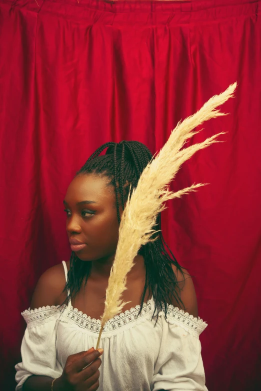 a woman holding feather next to a red curtain